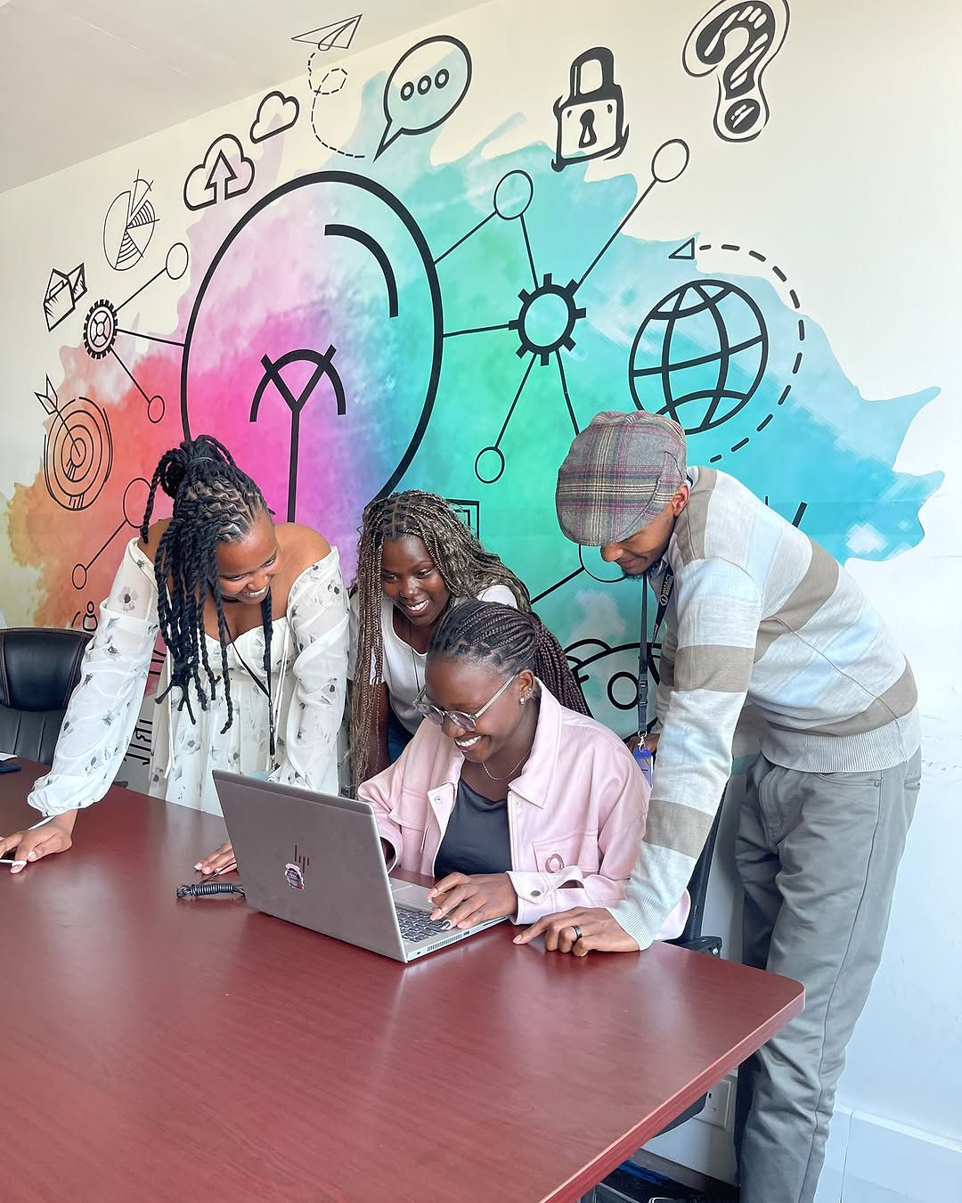 Four Impact Outsourcing team members gathered around a laptop on the Nairobi delivery floor, reviewing a live annotation task.